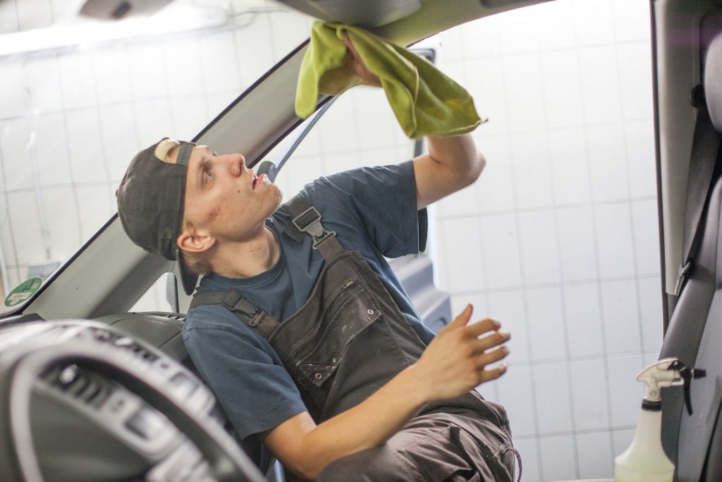 Mitarbeiter:in der Fahrzeugpflege reinigt mit einem Tuch den Innenraum eines Fahrzeugs.